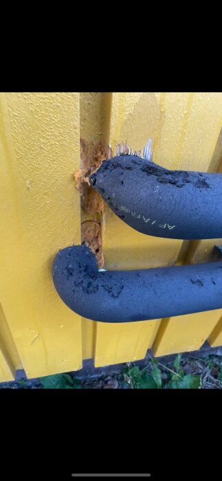 Rör med svart armaflex-isolering som skadats kring ojämnt hål i gul panel; synligt fogskum och vittrat isoleringsmaterial.