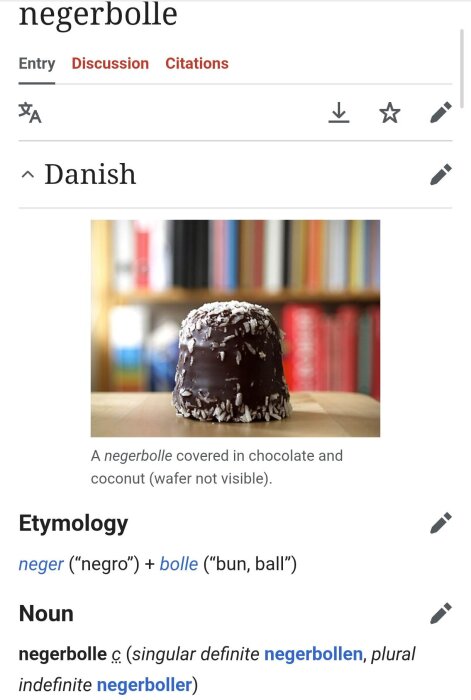 Chokladdoppad boll med kokosflingor på en bordsskiva, omgiven av suddiga bokhyllor i bakgrunden.