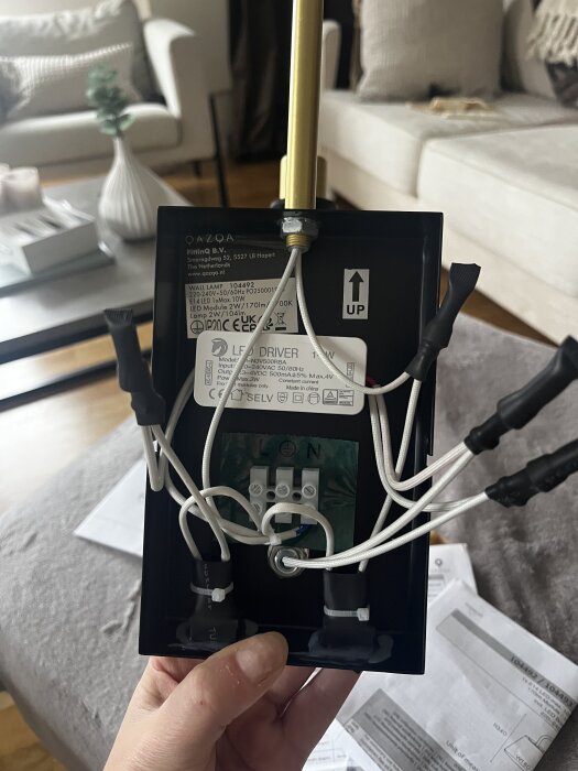 QAZQA Renier vägglampa baksida med synliga ledningar och anslutningsdetaljer, hålls i en hand i ett vardagsrum.