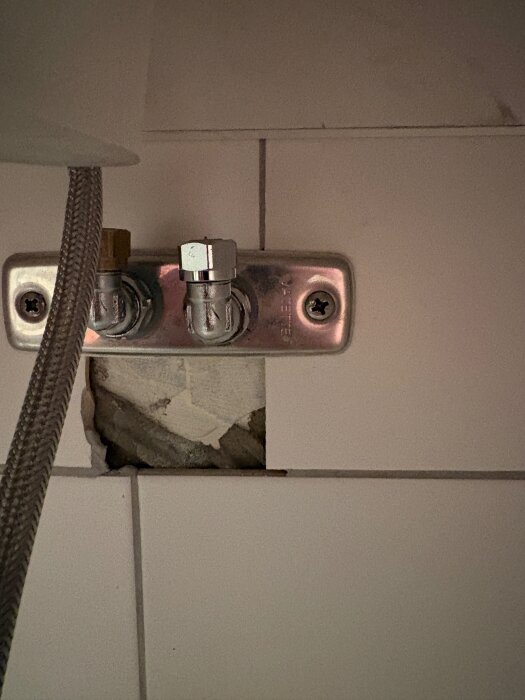 Rörkoppling med två ventiler och synliga fästen på kaklad vägg, problem med läckage mellan olika rörstorlekar.