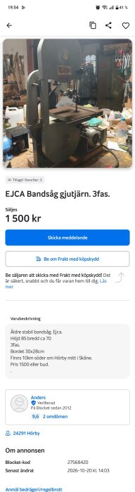 Äldre bandsåg av märket EJCA i gjutjärn, står på en arbetsbänk i en verkstad med verktyg på väggarna och hyllor fulla med diverse föremål.