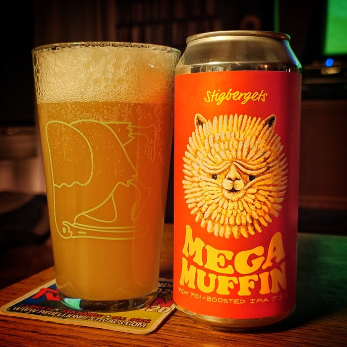 Ölglas med disig IPA bredvid en burk "Mega Muffin" IPA från Stigbergets, etikett med kattansikte.