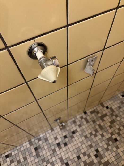 Vattenledning på kaklad vägg med mosaikgolv i en gäst-wc i ett 60-talshus, redo för renovering.