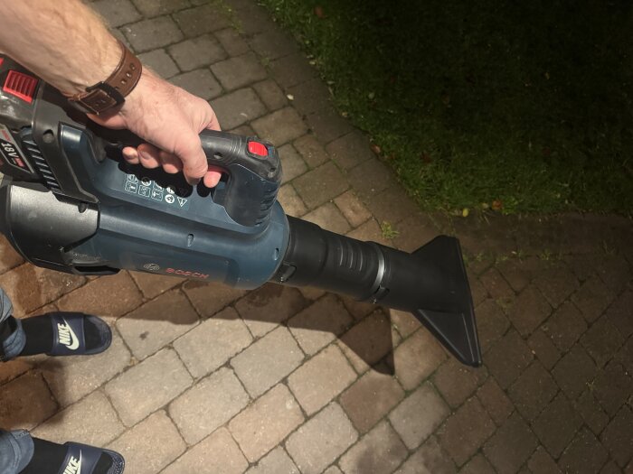 En person håller i en Bosch dammsugare med en förlängare, ståendes på en stengång.