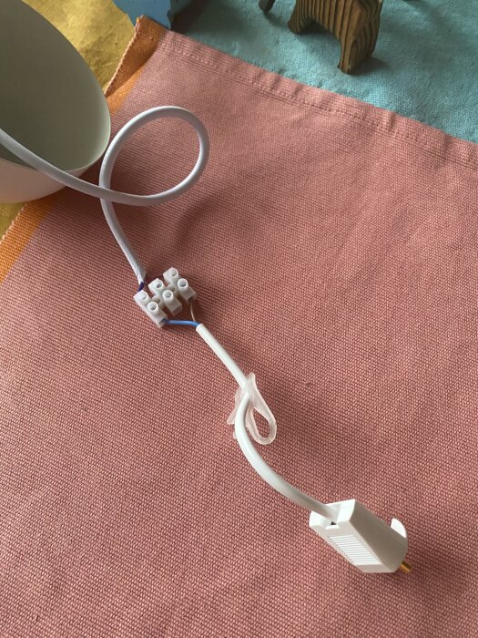 En sladdanslutning med kopplingsklämma och vit kabel mot en färgglad bakgrund.