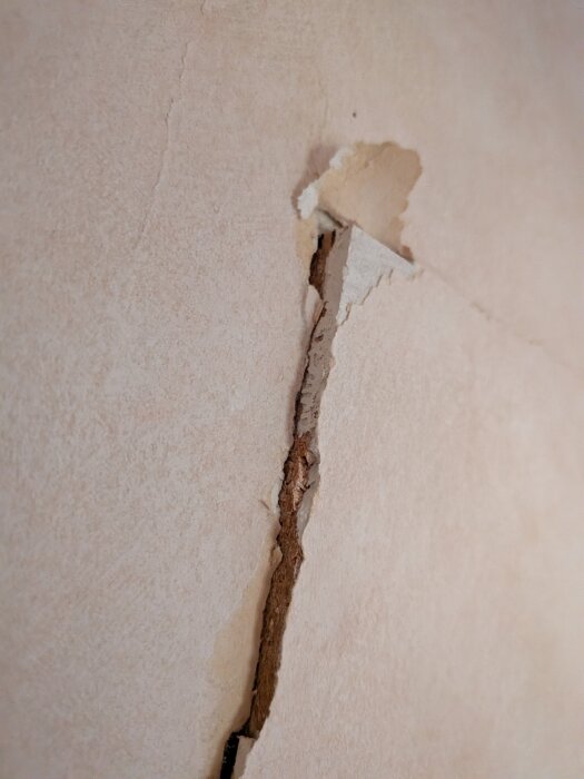 Sprucken tapet runt en igensatt dörröppning, visar hur väggen står ut en centimeter och basen ser ut att vara spånskiva.