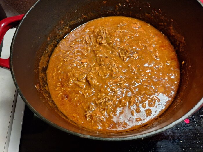 Köttfärssås i en röd gryta på spisen, nylagad som del av dagens middag med pasta och morötter.