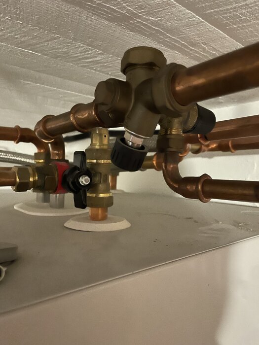 Rörsystem med kopparledningar och svarta vred nära en värmepump. Användaren söker råd om hur man fyller på vatten till värmepumpen.