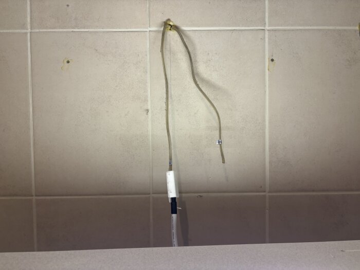 Lösa kablar på väggen, en med ström, bredvid hål genom kakel, efter elektrikerbesök för omdragning och korrekt inkoppling i skåp.