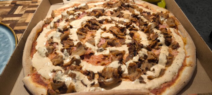Pizza med kebabkött och sås i en pizzakartong.