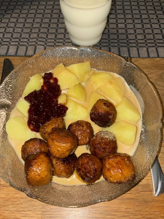 Tallrik med köttbullar, potatis, kantarellsås och lingonsylt, med ett glas mjölk.