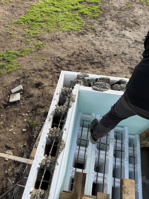 En person står på en nyligen gjuten betongvägg och inspekterar arbetet med synliga förstärkningsjärn och gjutfogar i solen.