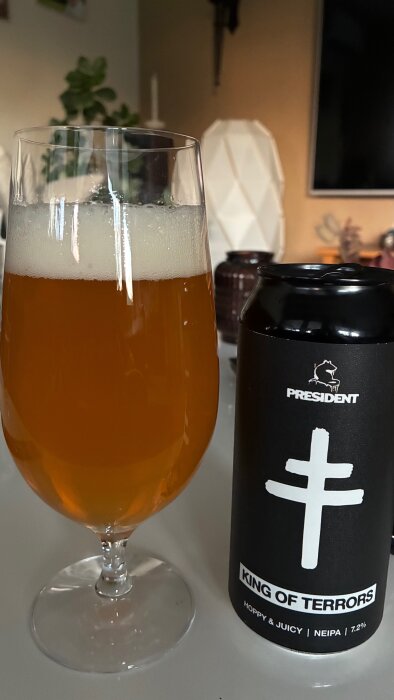 Ett glas öl av sorten "King of Terrors" NEIPA från President, bredvid en svart ölburk.