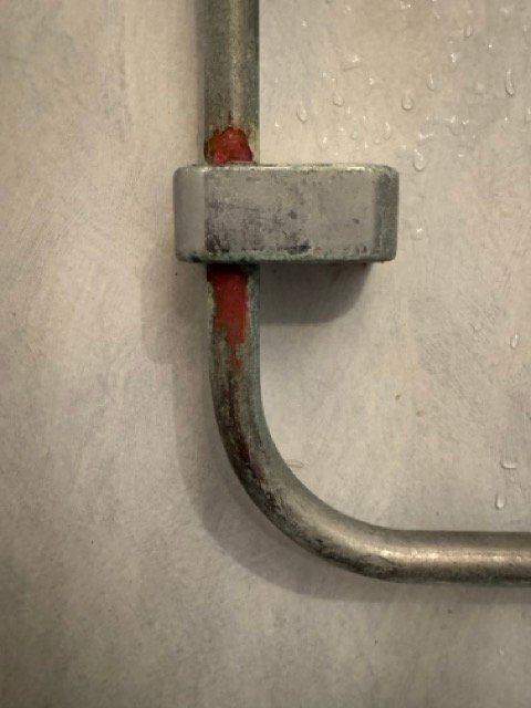 Varmvattenrör på en vägg med tecken på ärgning och korrosion, närbild. Röret går genom ett metallfäste.