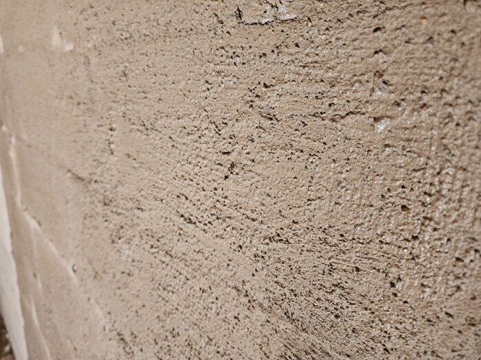 Närbild av en vägg med nyligen applicerat slam. Texturen ser grov ut, förberedd för påläggning av puts i nästa fas av renoveringen.