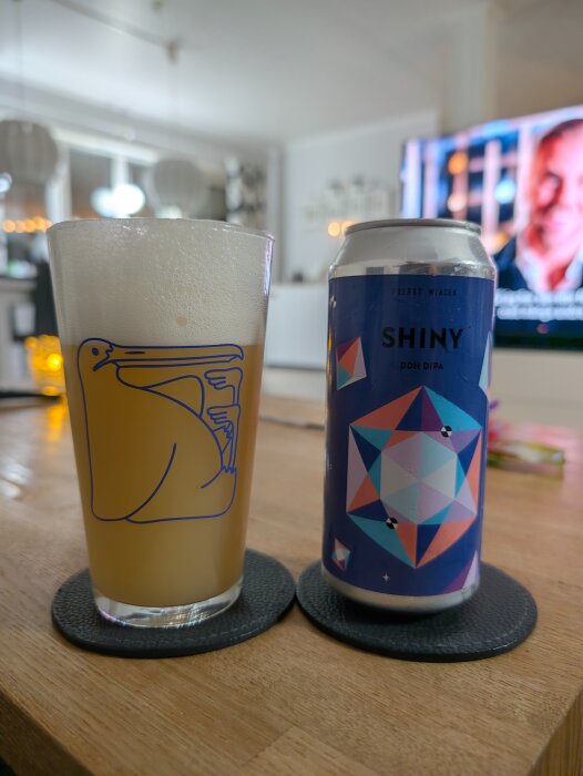 Ett glas öl med skum bredvid en burk med etikett "Fuerst Wiacek - Shiny" på ett bord inomhus.