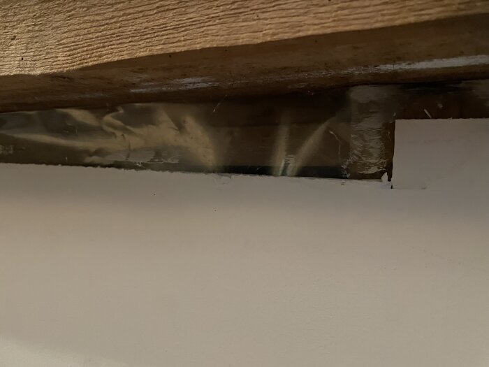Hål i gipsskiva nära taket, delvis täckt av plast, med trä bakom.