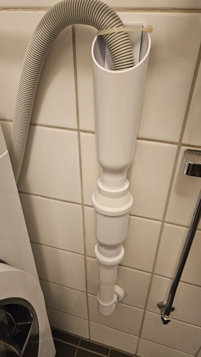 Tvättmaskinens avloppsslang ansluten till väggen med ett avloppsrör och vattenlås, observerad i en diskussion om dålig lukt.
