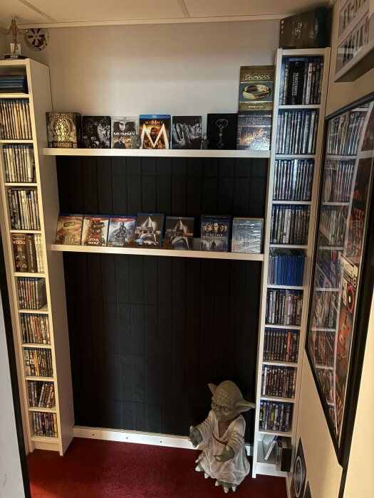 Hylla med DVD-filmer och Blu-ray, dekorerad med filmomslag från bland annat "The Mummy". En Yoda-figur står på röd matta längst ner.