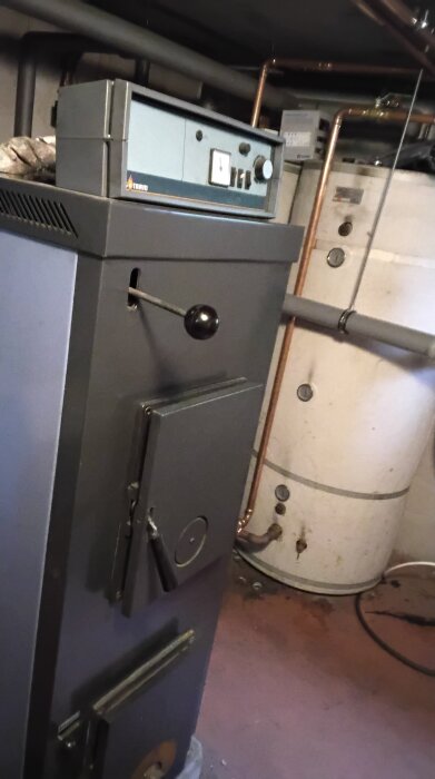 Vedeldad panna i källare, med kopparrör och tank intill.
