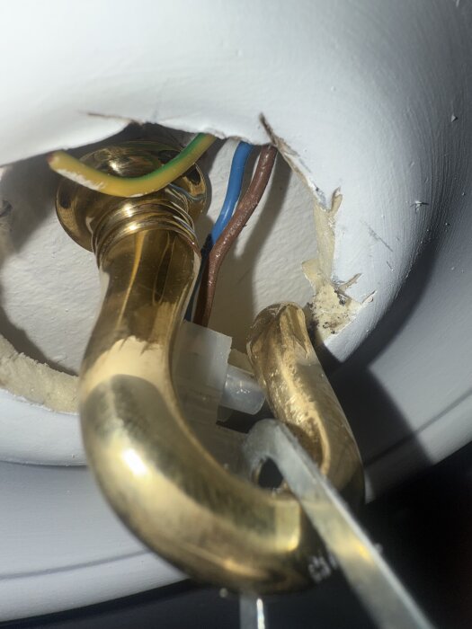 Gul/grön elektrisk kabel och koppling mot vit vägg eller tak, med mässingsdetalj i förgrunden.