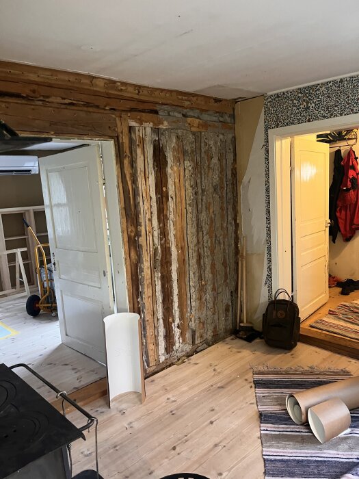 Renovering av kök pågår; en öppen vägg med delvis borttagna paneler, en dörr till hallen och diverse tillbehör ligger på trägolvet.