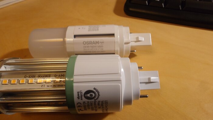 Två energieffektiva LED-lampor, en från Osram, ligger på ett träbord med text och märkningar synliga.