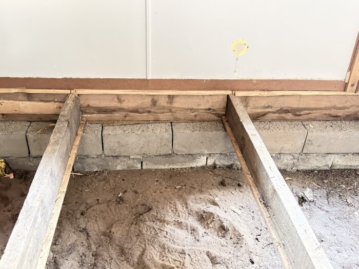 Träreglar på cementblock ovanpå jordgolv i en ouppvärmd krypgrund, delvis synlig trävägg ovanför blocken.