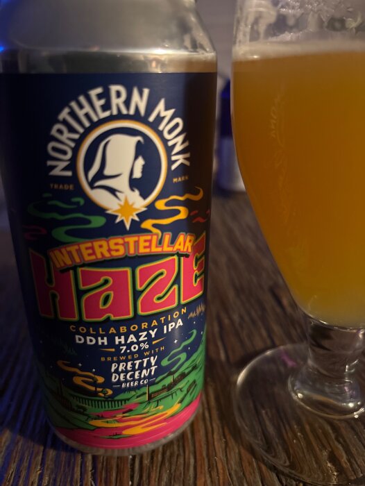 En burk Northern Monk Interstellar Haze DDH Hazy IPA och ett glas med samma öl på ett bord.
