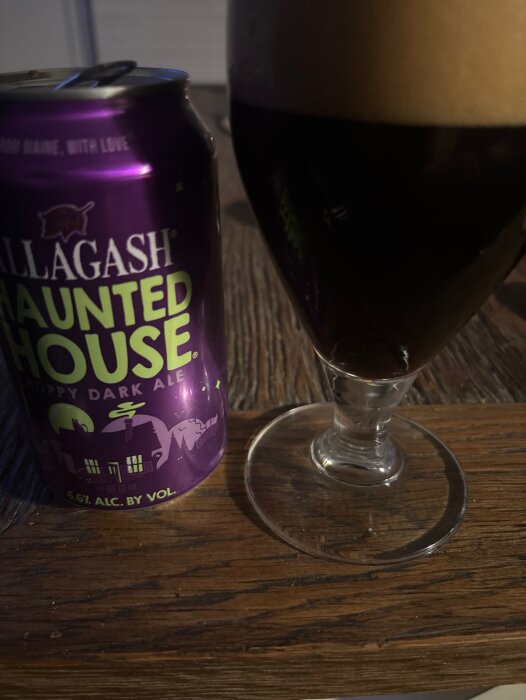En burk Allagash Haunted House hoppy dark ale bredvid ett glas med mörk ale på ett träbord.