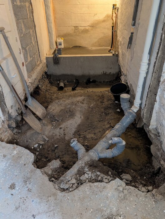 Grävning och rörarbeten i en källare, med exponerade rör och verktyg i en halvfärdig renoveringsmiljö.