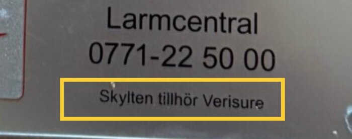 Verisure larmskylt med telefonnummer och texten “Skylten tillhör Verisure” i gulmarkerad ruta.