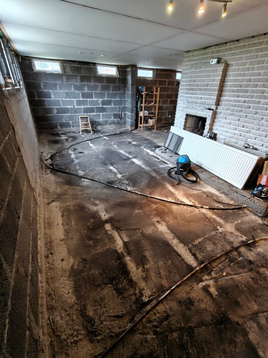 Ojämn golvplatta i en källare, tidigare täckt med tjära. Omgivande väggar av betongblock, gammalt trä har rivits ut.