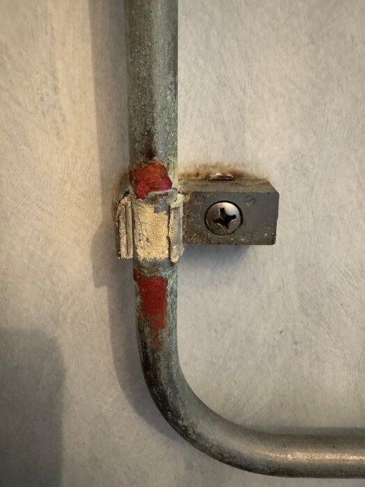 Korrosionsskadat rör med gammal, kornig beläggning kvar efter att hylsan tagits bort. Erodering syns på och under rör-hylsans fäste.