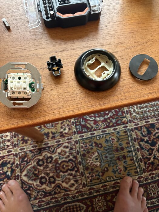 Elektriska komponenter och verktyg ligger utspridda på ett bord, inklusive en väggströmbrytare och en skruvmejselsats.