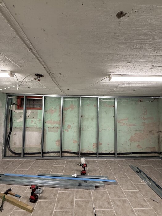 Renovering av källare med gipsväggar under arbete. Omonterade metallreglar och verktyg ligger på klinkergolvet.