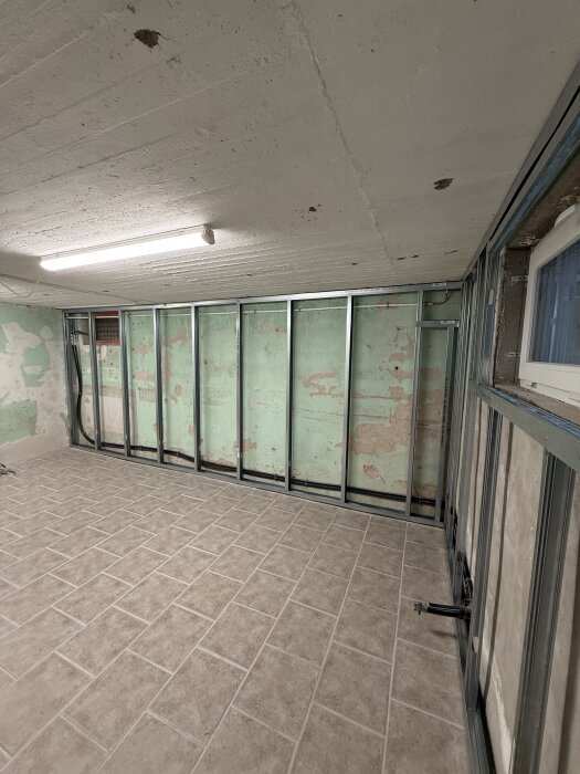 Renovering av rum med delvis färdigställs isoleringsramar och nyinstallerat kakelgolv, under takbelysning.