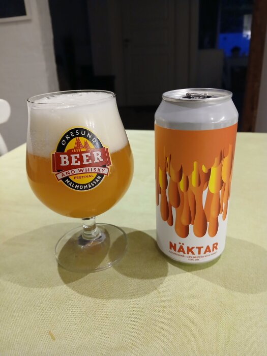 Glas med öl och burk med texten "Näktar", en DIPA från ett bryggeri, står på ett bord med ljus duk.