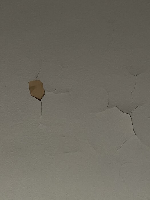 Spruckna innertak i ett putsat radhus från 50-talet, med synliga färgsprickor och en bit som fallit av, vilket undersöks för renovering.