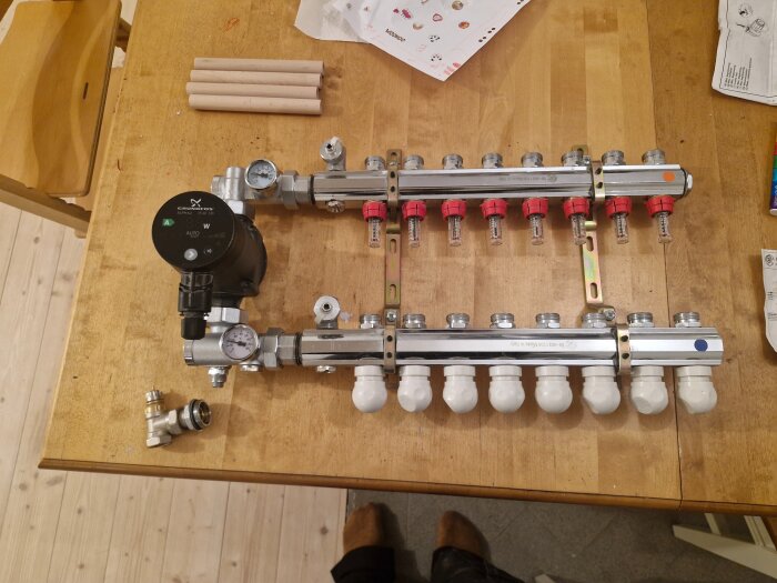 Golvvärme shuntgrupp med Grundfos pump, anslutna fördelningsrör och mätare, placerad på ett träbord.