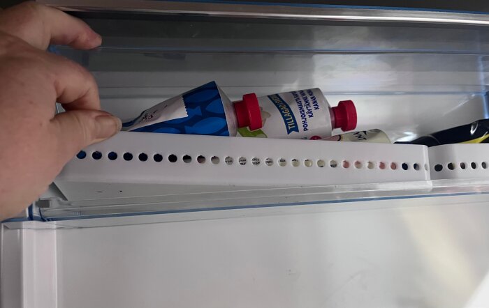 En hand öppnar en 3D-printad behållare i kylskåpsfacket, fylld med tuber, som förhindrar innehåll att ramla ut vid öppning.