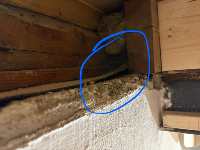Knutpunkt mellan mur och syllpapp i ett innertak, med en blå cirkel markerar ett område där pappen är ojämn och det drar kallt.
