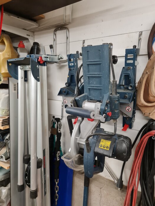 Väggmonterad såg och stativ hänger på krokar i garage, fastsatta på brädor på väggen för att fördela vikten på enkelgips.