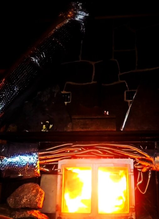 Brinnande eld i en kamin med stenväggar i bakgrunden, värmerummet för en vedeldad värmepump.