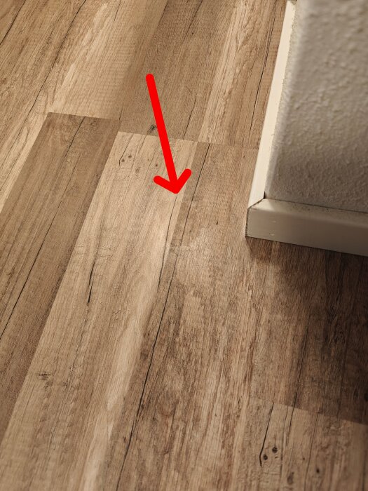 Laminatgolv med ljus fläck där ytan verkar ha lösts upp, röd pil markerar området.