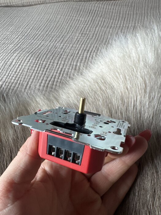 En ELKO Plus 315 LED-dimmer hålls i handen, visar baksidan med anslutningar och metallplatta.