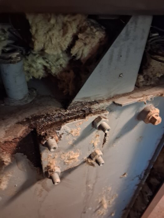Skadad pannkonstruktion med rostiga bultar och trasig isolering, upptäckt läcka som ska fixas med svetsning.