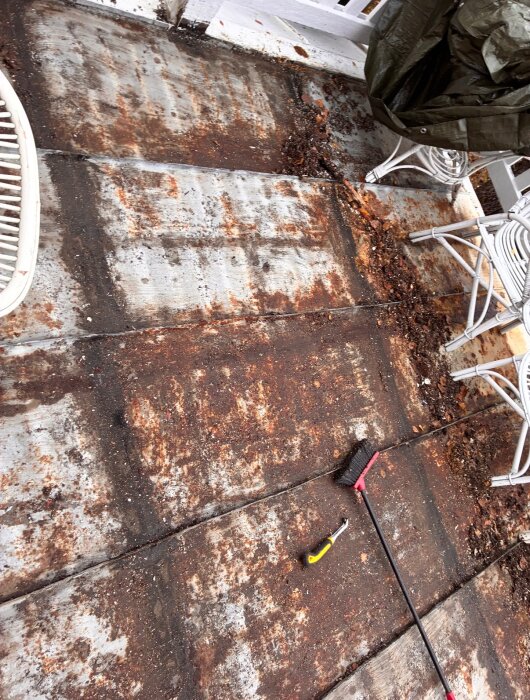 Rostigt plåttak med läckage och skräp, utrustat med verktyg som en borste och spade, möbler ovanpå som del av renovering av veranda.