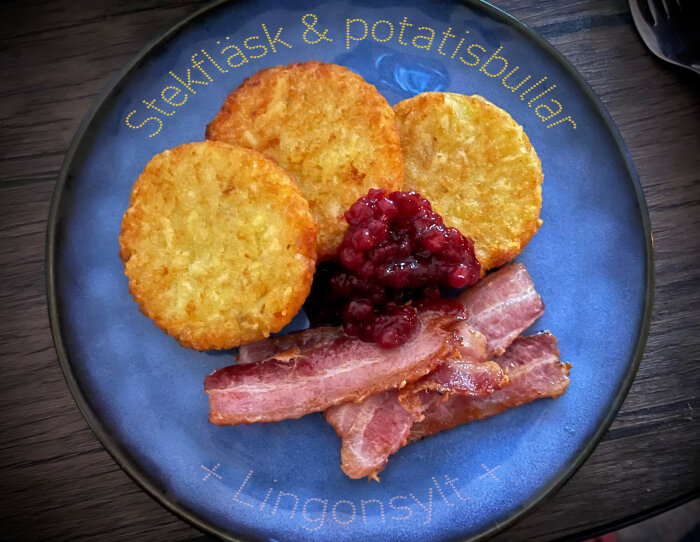 Tallrik med stekfläsk, potatisbullar och lingonsylt, serverat mot en mörk bakgrund.
