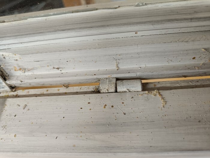 Närbild av koppelbeslag på en fönsterkarm, slitet trä med spår av gammal färg; verktyg för fönsterrenovering behövs för att demontera beslag.